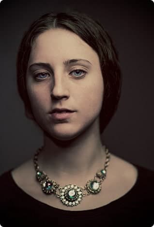 Moody portrait of a woman with dark updo and statement necklace, dark background.