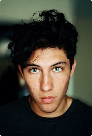 Young man with messy dark hair and bright blue eyes, close-up.