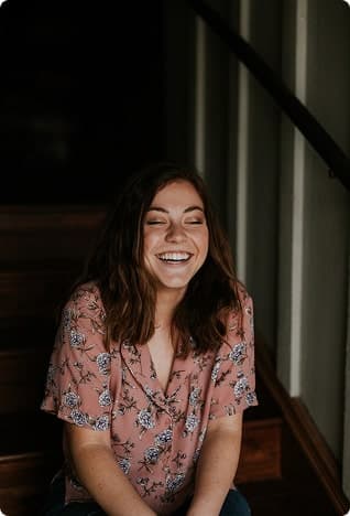 Woman in a floral blouse sitting on stairs, smiling.