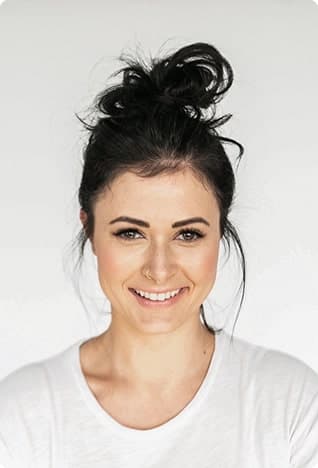Woman with a high bun in a white top, beaming smile, bright background.
